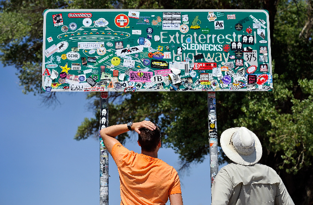 Tourist Floris Otten, left, of The Netherlands, and Dean Baumgartner, of Adventure Photo Tours look over all the stickers covering the Extraterrestrial Highway sign on Tuesday, Aug. 5, 2014. Baumg ...