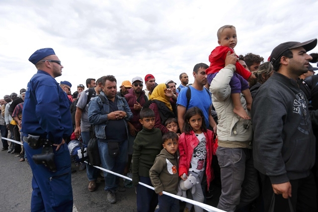 A Hungarian policeman observes migrants as they wait for buses in a makeshift camp at a collection point in the village of Roszke, Hungary, September 7, 2015. (Reuters/Laszlo Balogh)