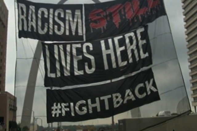 Activists raised a banner in downtown St. Louis on Monday, August 10, 2015, that read "Racism still lives here. #fightback" as part of the Ferguson Commemoration Weekend‘s day of c ...
