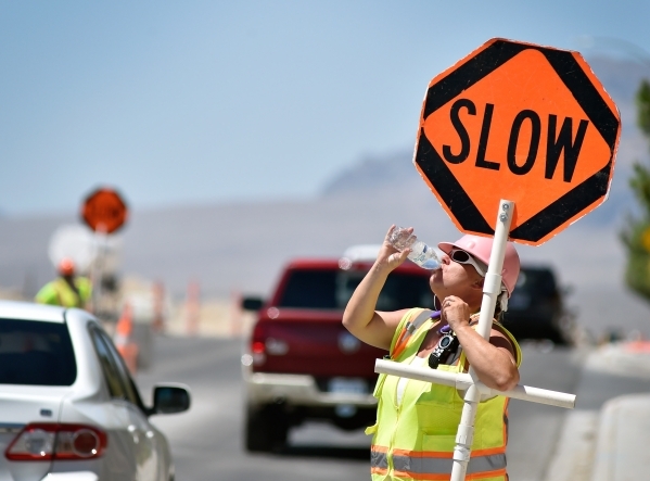 Flagger Shayne Boley takes a drink of water as she guides vehicles though a construction zone on North Grand Canyon Drive in Las Vegas on Tuesday, June 16, 2015. Boley drinks a dozen bottles of wa ...