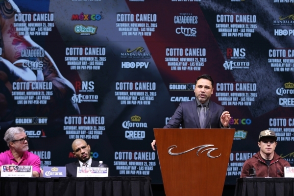 Boxing promoter Oscar De La Hoya speaks at the podium as boxing trainer Freddie Roach, from left, Miguel Cotto and Saul "Canelo" look on during the final press conference for the fight b ...