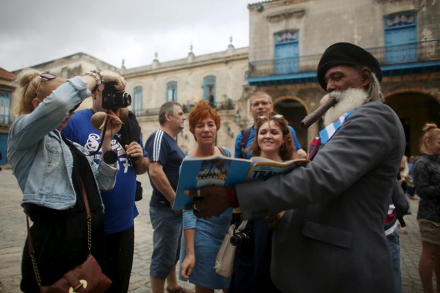 Hermenegildo Arensivia, 61, (R), shows pictures of him in a magazine to tourists from Poland in old Havana in this January 13, 2016 picture. REUTERS/Alexandre Meneghini