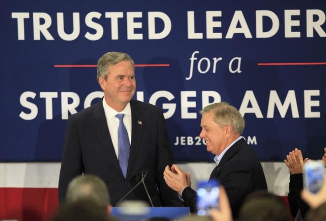 Jeb Bush (L) is applauded by U.S. Senator Lindsey Graham (R) as he arrives to announce that he is ending his campaign for the White House by suspending his campaign for the Republican presidential ...