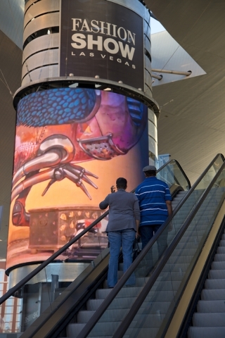Visitors ascend an escalator near one of the massive screens recently added to the pillars underneath the "Cloud," a steel canopy at the Fashion Show Mall on the Las Vegas Strip ...