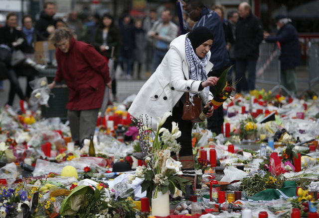 A woman helps re-adjust the tributes left for the victims of the recent bomb attacks in Brussels following heavy rain in the Place de la Bourse in Brussels, Monday, March, 28, 2016. The Belgian he ...