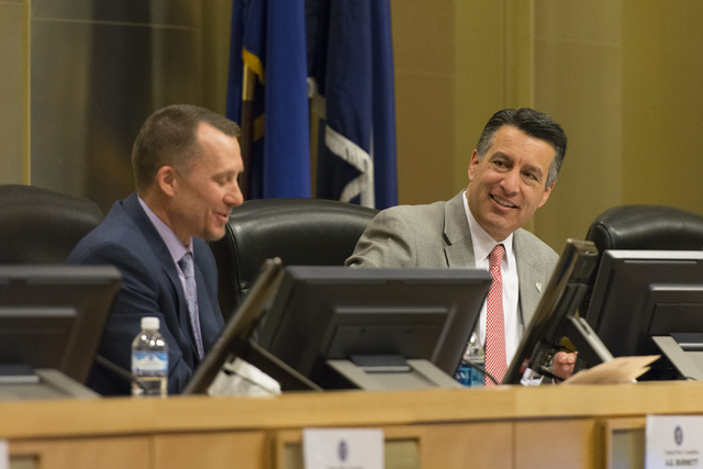 A.G. Burnett, chairman of the Nevada Gaming Control Board, left, and Nevada Governor Brian Sandoval speak at the Nevada Gaming Policy Committee meeting at Las Vegas City Hall Council Chambers Mond ...