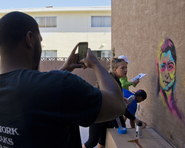 Brandon Russell, a resident at a New Genesis Transitional Housing apartment complex, takes a photo as the Gaels Give Hope organization from Bishop Gorman High School paints murals during a volunte ...