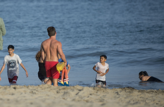 In this Sunday, May 29, 2016, photo, a lifeguard warns beach goers to stay out of the water at Corona del Mar beach in Newport Beach, Calif. Thousands of Memorial Day beachgoers were kept out of ...