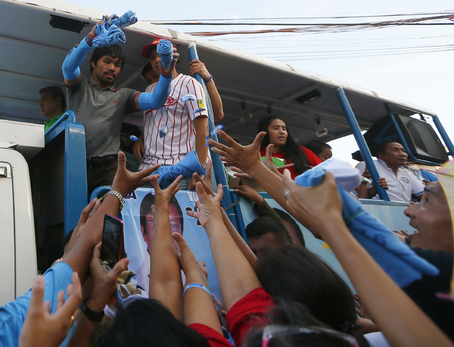 Filipino boxer and Congressman Manny Pacquiao, who is running for senator in Monday's national elections, throws souvenir t-shirts, candies and wrist bands to supporters during his campaign sortie ...