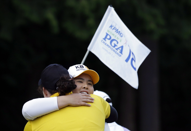 The flag for the 18th hole is carried past as Inbee Park, of South Korea, is embraced after finishing the first round at the Women's PGA Championship golf tournament at Sahalee Country Club Thursd ...