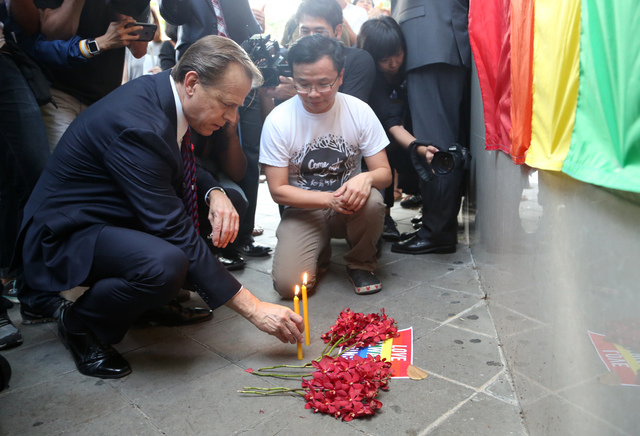 The U.S. ambassador to Thailand, Glyn T. Davies, places a candle with vigil organizer Paisam Likhitpreechakul outside the U.S. Embassy in Bangkok for those killed and wounded in the Sunday mass sh ...