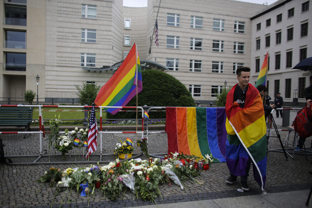 A man stand next to flowers placed in front of the U.S. embassy during a vigil in Berlin, Monday, June 13, 2016, to honor the victims of the attack on the gay nightclub in Orlando, Fla.  (Markus S ...