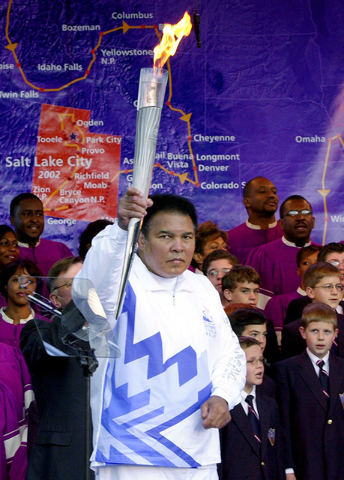 Boxing legend Muhammad Ali holds up the first Olympic torch lit from the cauldron in front of a map showing the torch's route during a ceremony at Centennial Olympic Park in Atlanta Tuesday, Dec.  ...