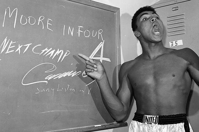 In this Nov. 15, 1962, file photo, young heavyweight boxer Cassius Clay, who later changed his name to Muhammad Ali,  points to a sign he wrote on a chalk board in his dressing room before his fig ...