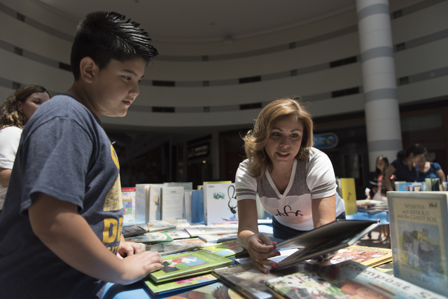 Stevie Escalante, 9, left, is shown a book by Amarilis Rosario-Tillema, a volunteer with the National Charity League's Green Valley chapter, during the Clark County School District's Reading Range ...