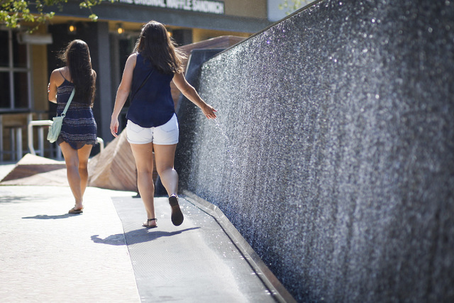 Olivia Eisman, 24, center, drags her hand trough a decorative waterfall in triple-digit heat while following her friend Erica Chavez, 24, left, near the New York-New York hotel-casino on the Strip ...