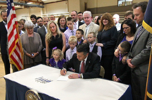 Nevada Gov. Brian Sandoval signs an anti-bullying bill into law at Carson Middle School in Carson City, Nev., on Wednesday, May 20, 2015. Surrounded by lawmakers and the families of students who w ...