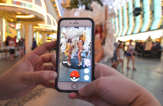 Review-Journal Digital News Editor Ashley Casper plays "Pokemon Go" as showgirls Cassandra, left, and Christa pose along the Fremont Street Experience in downtown Las Vegas on Wednesday, July 13,  ...