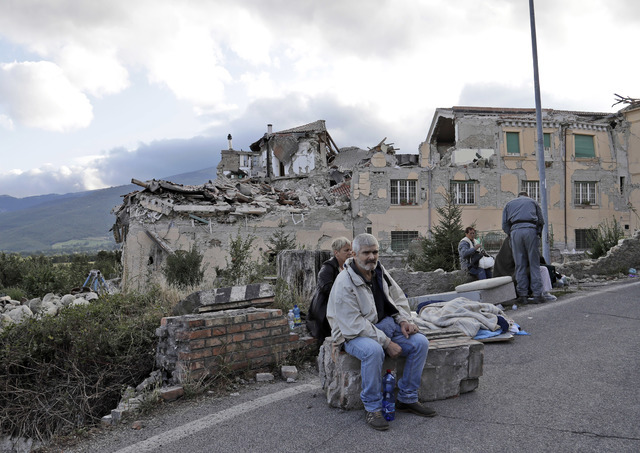 People sit on the side of a road as collapsed buildings are seen in the background following an earthquake, in Amatrice, Italy, Wednesday, Aug. 24, 2016.  (Alessandra Tarantino/AP)
