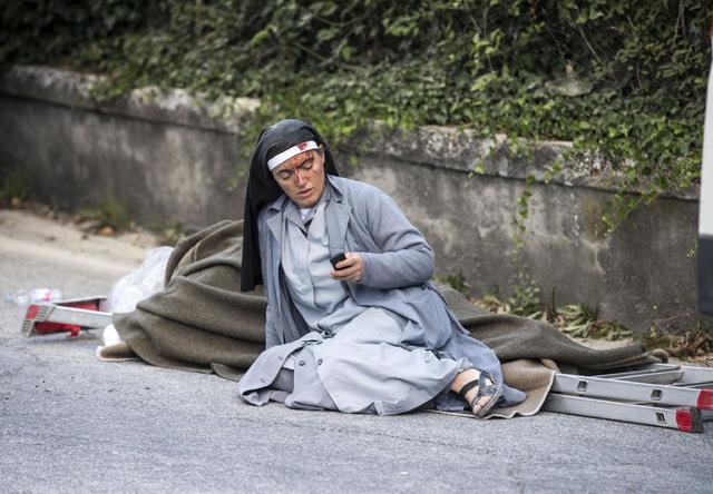 A nun checks her mobile phone as she lies near a victim laid on a ladder following an earthquake in Amatrice Italy, Wednesday, Aug. 24, 2016. (Massimo Percossi/ANSA via AP)