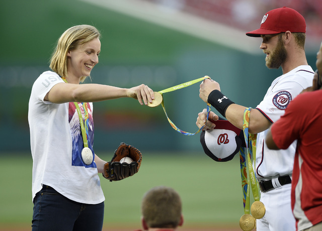 Olympic gold medal swimmer Katie Ledecky, left, hands her medals to Washington Nationals' Bryce Harper, right, to hold before she threw out the ceremonial first pitch before a baseball game betwee ...