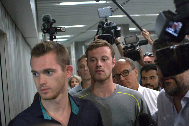 Journalists surround American Olympic swimmers Gunnar Bentz, left, and Jack Conger, center, as they leave the police station at Rio International airport early Thursday Aug. 18, 2016. The two were ...