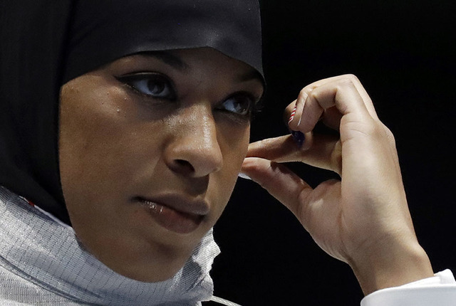 Ibtihaj Muhammad od the United States adjusts her hijab prior to competing with Olena Kravatska of Ukraine in the women's individual saber fencing event at the 2016 Summer Olympics in Rio de Janei ...