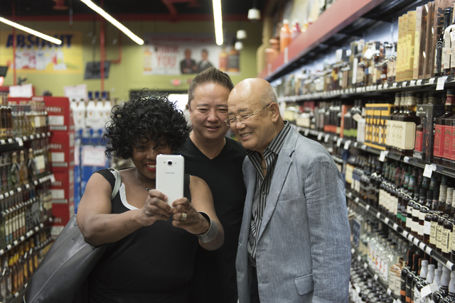 Rheata Porte, left, takes a selfie with Hae Un Lee, founder of Lee's Discount Liquor, right, and his son, Kenny Lee, president of the company, during the grand opening of the store at 1450 W. Hori ...