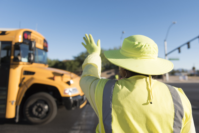 Crossing guard Patricia Bass waves to a school bus driver from her work site at Lake Mead Boulevard at Tonopah Drive before classes at West Preparatory Academy in Las Vegas, Thursday, Oct. 6, 2016 ...