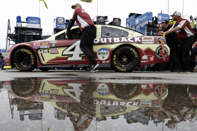 Crew members for NASCAR Sprint Cup driver Kevin Harvick (4) roll past standing rain water at Kansas Speedway in Kansas City, Kan., Friday, Oct. 14, 2016. (AP Photo/Colin E. Braley)