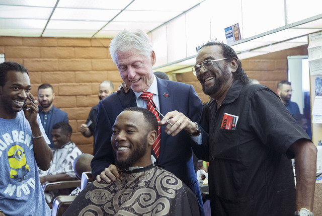 Former President Bill Clinton helps Mac Smith, Jr., right, owner of Hair Unlimited, cut D.J. Anderson's hair on Thursday, Nov. 3, 2016, in Las Vegas. President Clinton was in Las Vegas for a rally ...