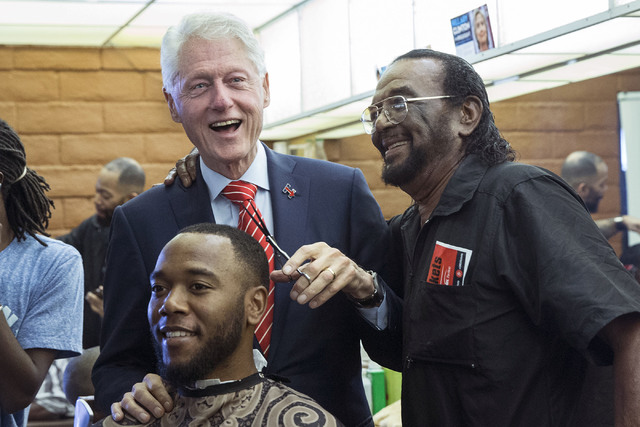 Former President Bill Clinton helps Mac Smith, Jr., right, owner of Hair Unlimited, cut D.J. Anderson's hair on Thursday, Nov. 3, 2016, in Las Vegas. President Clinton was in Las Vegas for a rally ...