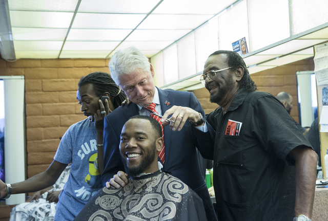 Former President Bill Clinton helps Mac Smith, Jr., right, owner of Hair Unlimited, cut D.J. Anderson's hair on Thursday, Nov. 3, 2016, in Las Vegas. President Clinton was in Las Vegas for a rally ...
