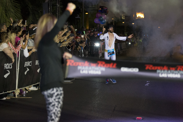 Michael Wardian in costume as Elvis raises his arms in victory as he completes the Rock-n-Roll Marathon for men in first place at the Strip near The Mirage hotel-casino on Sunday, Nov. 13, 2016, i ...