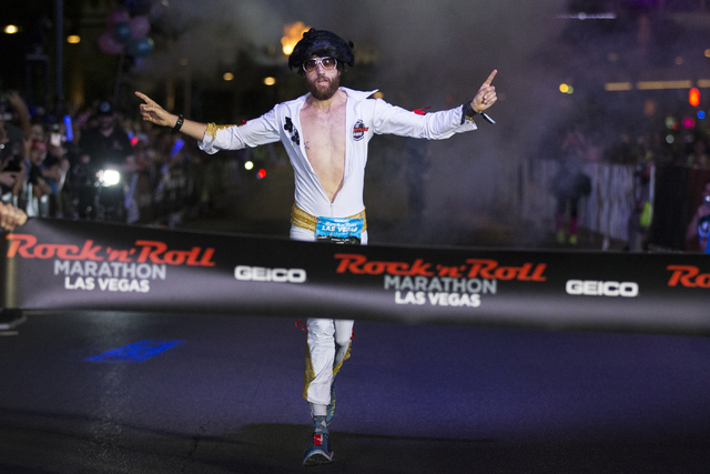 Michael Wardian in costume as Elvis raises his arms in victory as he completes the Rock-n-Roll Marathon for men in first place at the Strip near The Mirage hotel-casino on Sunday, Nov. 13, 2016, i ...