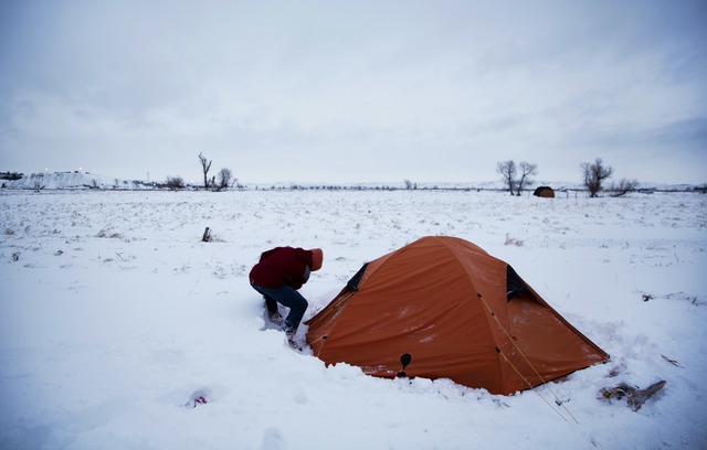In this Wednesday, Nov. 30, 2016 photo, Roy Tom of Ontario, Canada, and a member of the Ojibwa Native American tribe clears away snow from his tent where he's lived for over two months at the Ocet ...