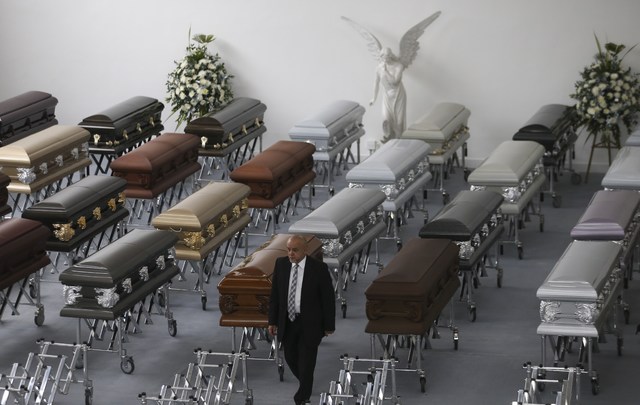 A funeral employee walks past coffins containing the remains of the victims of the Colombian air tragedy are lined up in the parking garage of the San Vicente funeral home in Medellin, Colombia, T ...