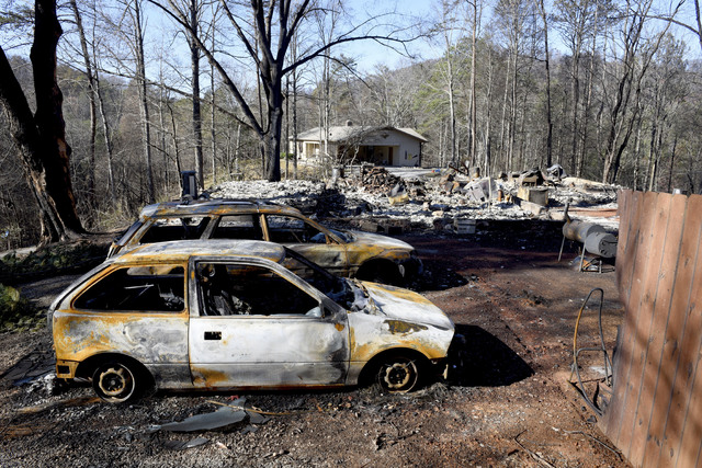 Charred home and cars sit on a property, while a neighbor's home, background, is undamaged Thursday, Dec. 1, 2016, in Gatlinburg, Tenn. (Michael Patrick/Knoxville News Sentinel via AP)