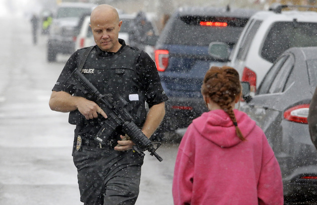 A police officer carries his weapon as he walks along the street in front of Mueller Park Junior High after a student fired a gun into the ceiling Thursday, Dec. 1, 2016, in Bountiful, Utah. (Rick ...