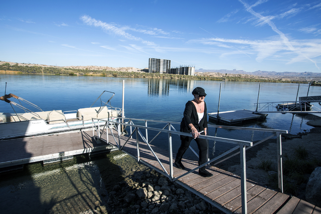 Susan Martinolich walks on her dock in Bullhead City, Ariz. while the abandoned Emerald River resort tower is seen in the background on Tuesday, Dec. 6, 2016. The project has been shut down for al ...