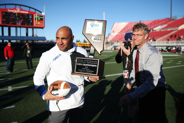 Bishop Gorman's head football coach Kenny Sanchez is presented the champion trophy by Bart Thompson, executive director for the Nevada Interscholastic Activities Association, after their 84-8 win ...