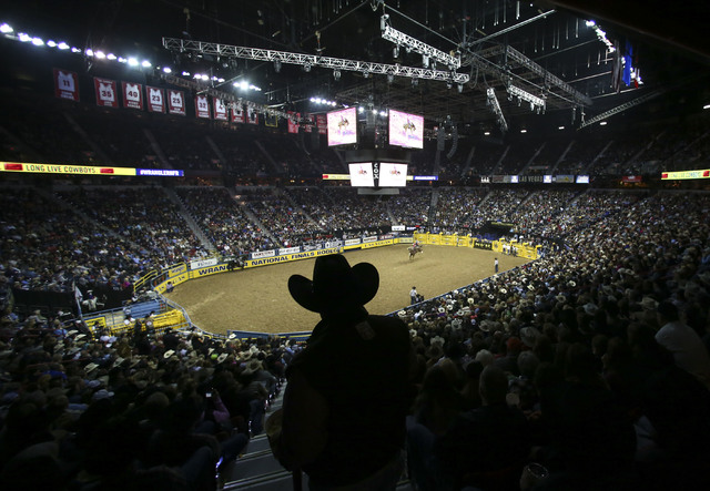 An attendee watches as Zeke Thurston rides Killer Bee while competing in the saddle bronc riding event during the 2nd go-round of the National Finals Rodeo at the Thomas & Mack Center in Las V ...