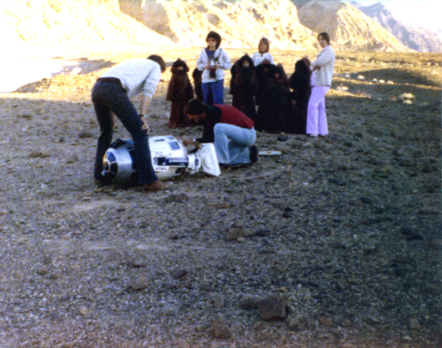 Film crew members work on R2-D2 as a group of Jawas recruited from Death Valley Elementary School look on during the production of &quot;Star Wars&quot; in January 1977. (Sally Weber)