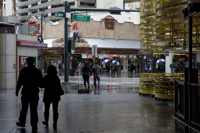 Puddles fill the street near the Fremont Street Experience as pedestrians walk under covered walk ways or with umbrellas on Saturday, Feb. 18, 2017, in downtown Las Vegas. On Friday a flash-flood  ...