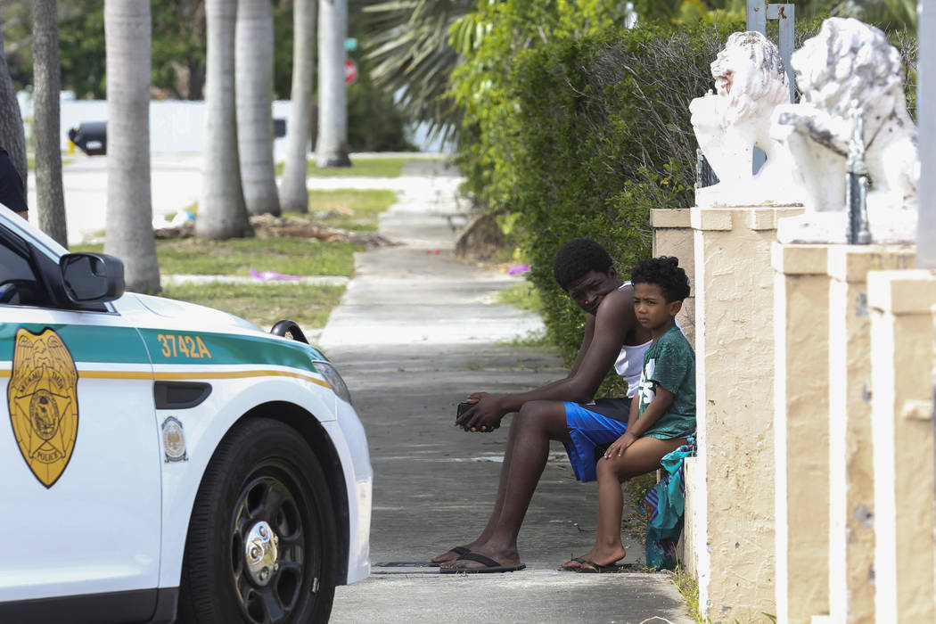 Suspected squatters sit outside a Miami house after Miami-Dade police officers removed them from the property on Tuesday, April 18, 2017. Matias J. Ocner