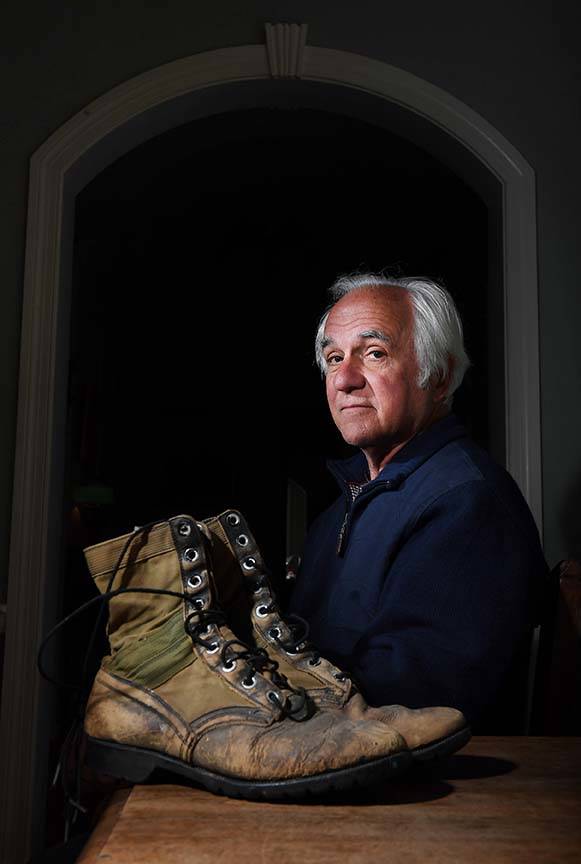 George Chaconas sits next to boots he wore in Vietnam at his home in Washington. (Matt McLain/The Washington Post)