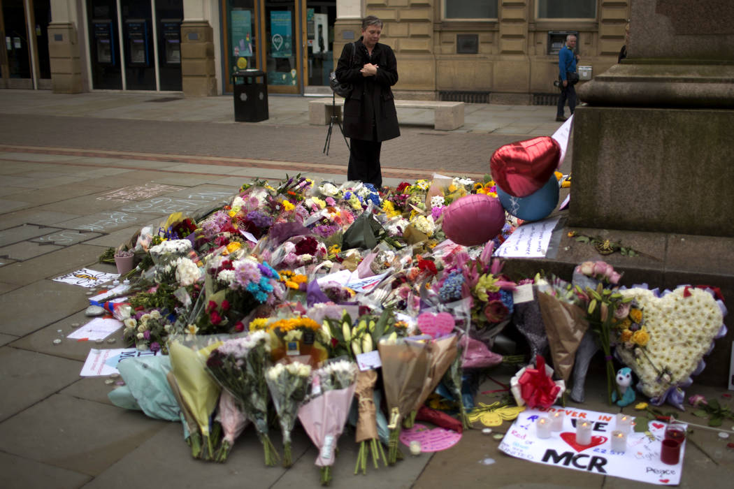 A woman stands next to flowers offered for the victims of a suicide attack at a concert by Ariana Grande that killed more than 20 people Monday night in central Manchester, Britain, Wednesday, May ...