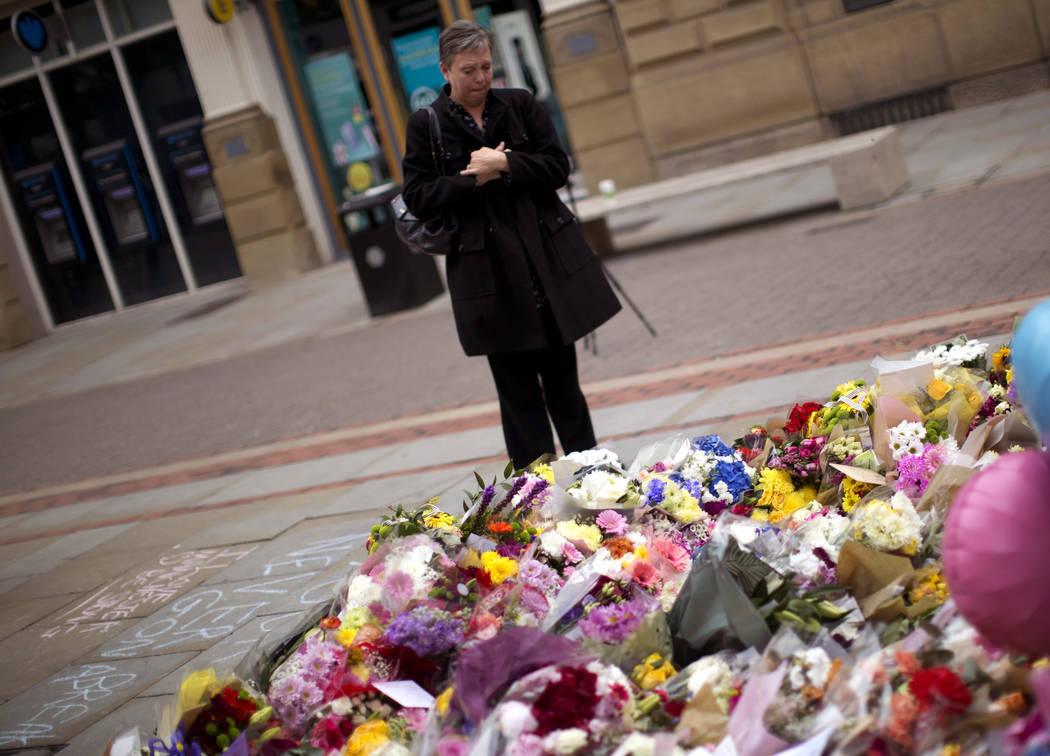 A woman stands by flowers offered for the victims of a suicide attack at a concert by Ariana Grande that killed more than 20 people Monday night in central Manchester, Britain, Wednesday, May 24, ...