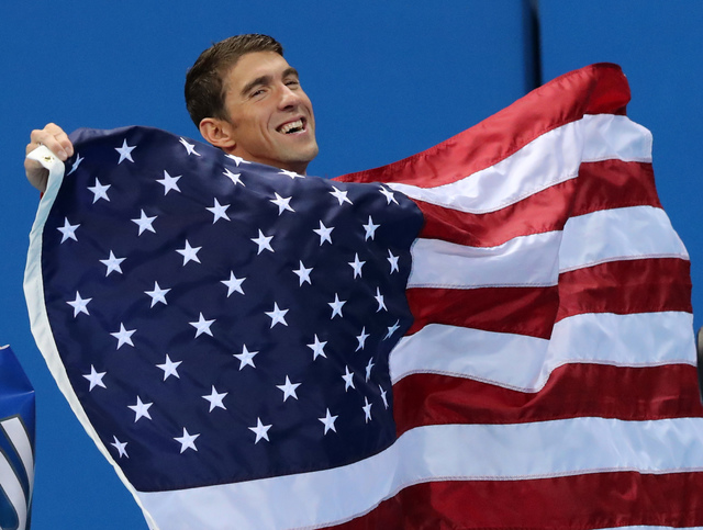 United States' Michael Phelps walks with his national flag during the medal ceremony for the men's 4 x 100-meter medley relay final during the swimming competitions at the 2016 Summer Olympics, Su ...