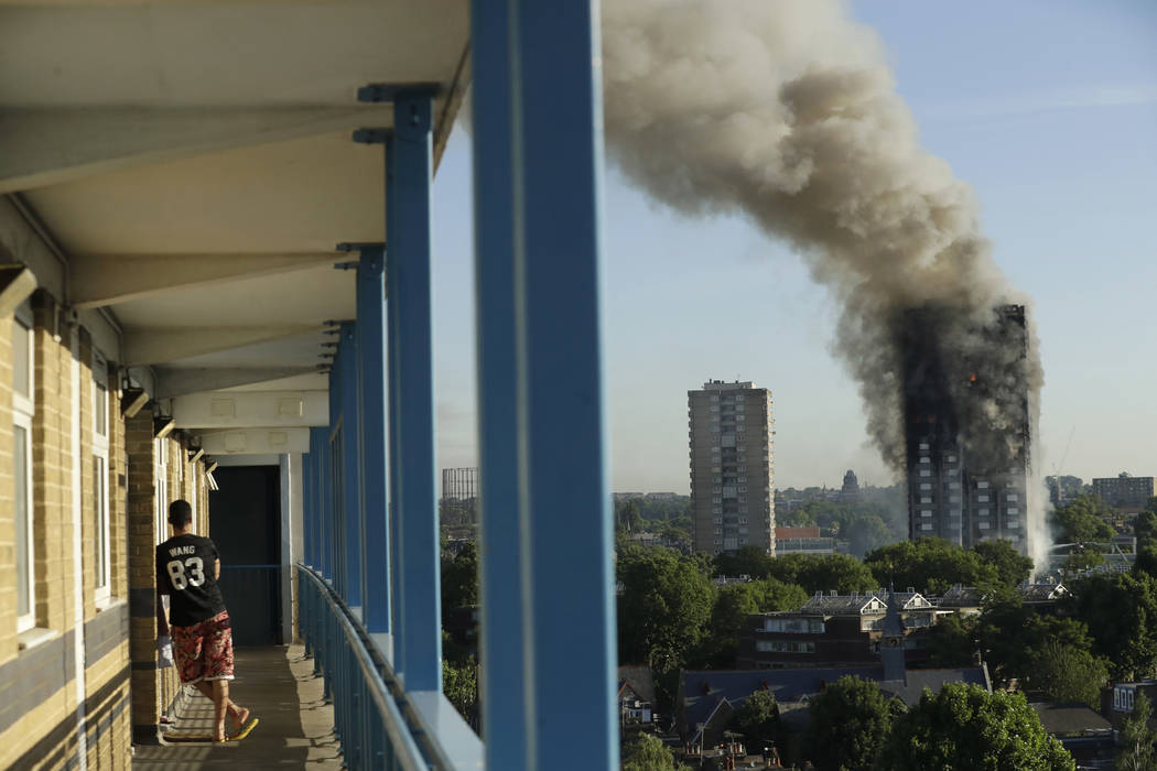 A resident in a nearby building watches smoke rise from a building on fire in London, Wednesday, June 14, 2017. A massive fire raced through the 27-story high-rise apartment building in west Londo ...
